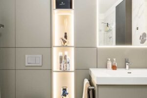 Koupelna s WC, podsvícenými policemi, závěsnou toaletou a umyvadlovou skříňkou v šedém odstínu.