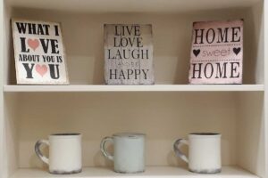 Dekorativní cedulky s nápisy Live Love Laugh a Home Sweet Home na zaplněné polici