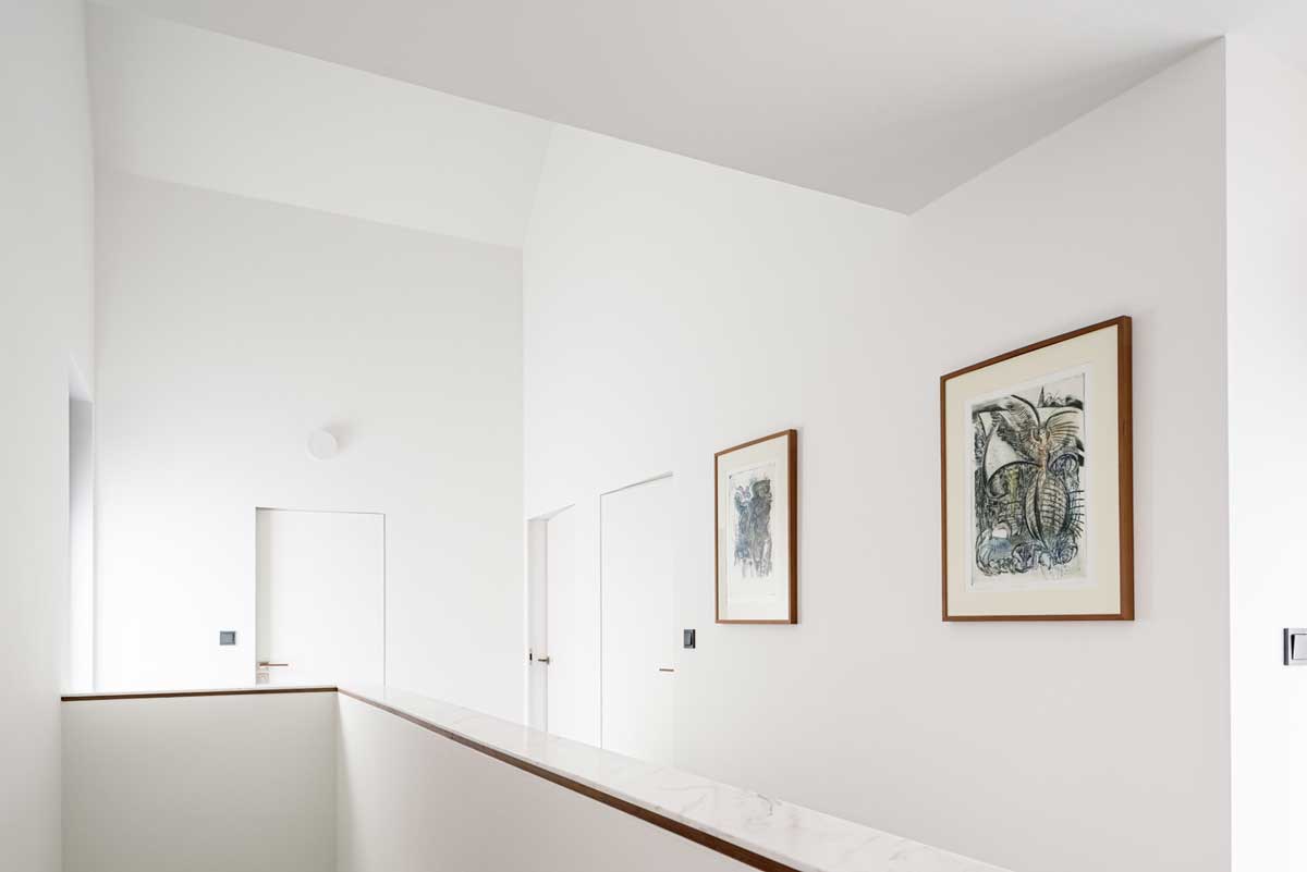 Světlá chodba v horním patře s bílými stěnami, dřevěnými detaily a barevnými uměleckými obrazy.