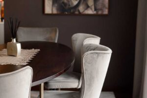 Detail jídelního prostoru s čalouněnými židlemi, tmavým dřevěným stolem a uměleckým obrazem na stěně.