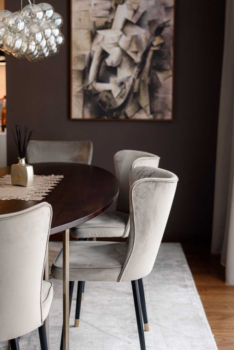 Detail jídelního prostoru s čalouněnými židlemi, tmavým dřevěným stolem a uměleckým obrazem na stěně.