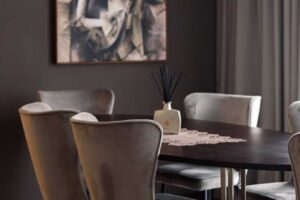 Detail oválného jídelního stolu z tmavého dřeva s jemnou dekorací a designovým svítidlem nad deskou.