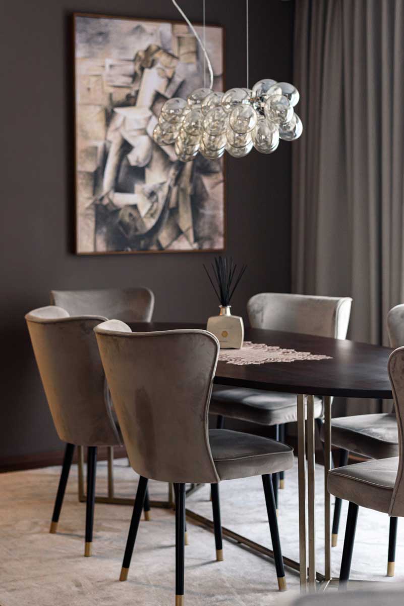 Detail oválného jídelního stolu z tmavého dřeva s jemnou dekorací a designovým svítidlem nad deskou.