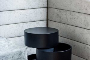 Designový odkládací stolek v černém matném provedení umístěný u čalouněného sezení v obytném prostoru.