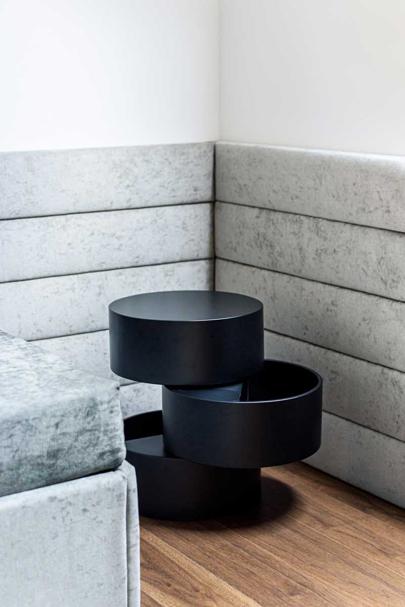 Designový odkládací stolek v černém matném provedení umístěný u čalouněného sezení v obytném prostoru.