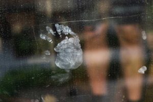 Dětský otisk ruky na skleněné ploše, na kterém je vidět mastnota a jemné šmouhy od prstů.