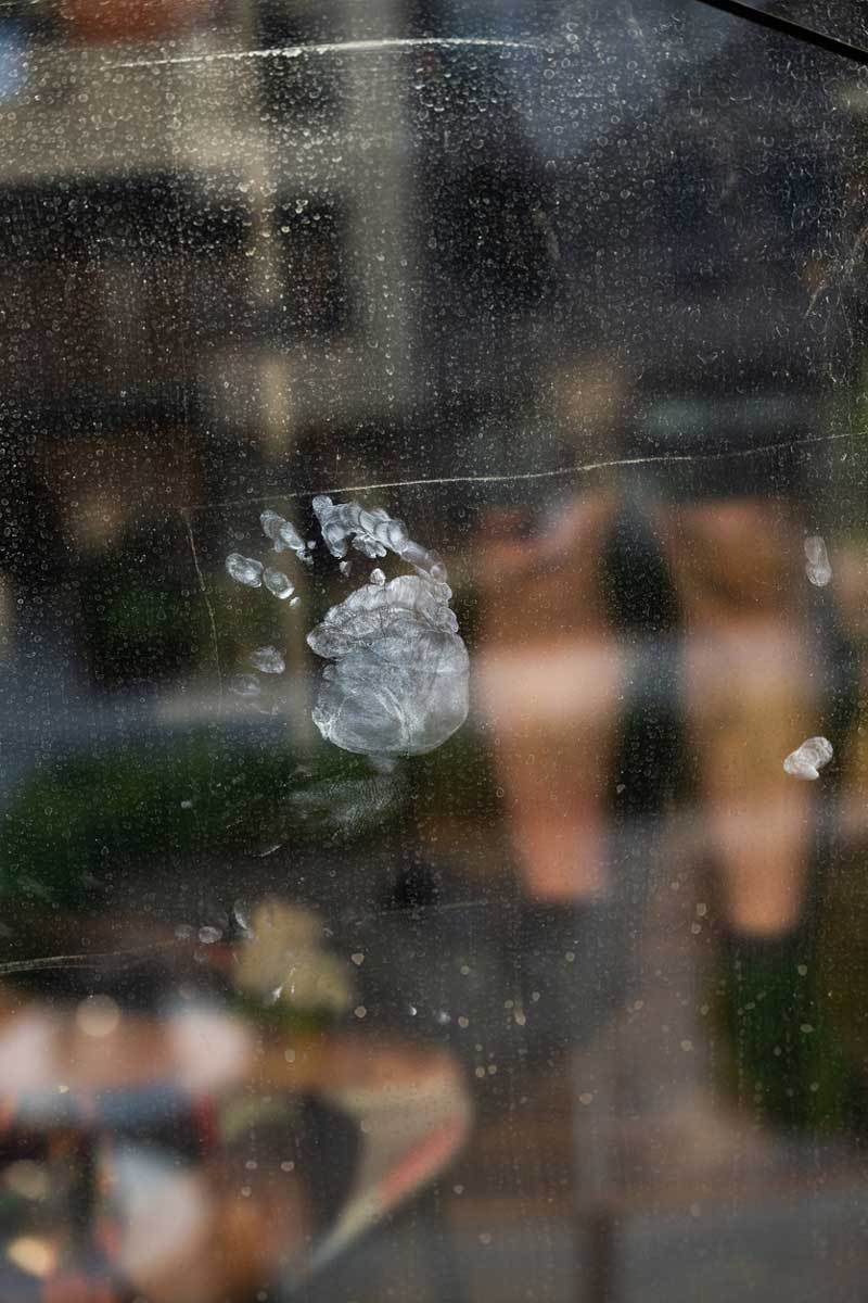 Dětský otisk ruky na skleněné ploše, na kterém je vidět mastnota a jemné šmouhy od prstů.