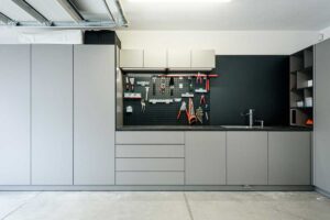 Garáž s vestavěným nábytkem na míru, úložnými skříněmi a kovovou stěnou na zavěšení nářadí.