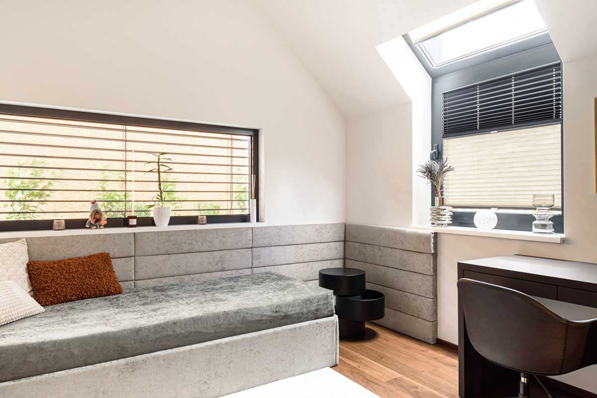 Pokoj pro hosty se zabudovaným sezením, jednoduchým pracovním koutem a světlým interiérem otevřeným do krovu.