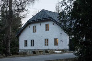 Pohled na zadní fasádu šumavské chalupy s kamennou podezdívkou a bílou omítkou