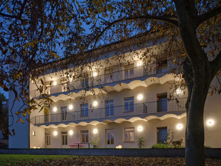 Večerní pohled na rekonstruovaný pavlačový dům s osvětlenými pavlačemi a klidnou atmosférou vnitrobloku