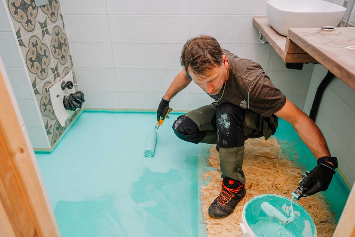 Nanášení hydroizolační vrstvy na podlahu koupelny před pokládkou dlažby
