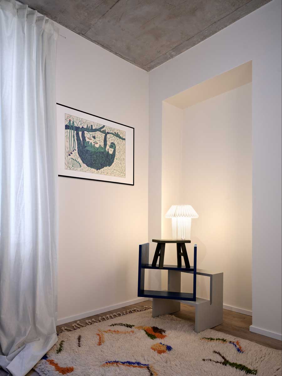 Interiér bytu v rekonstruovaném pavlačovém domě s odhaleným betonovým stropem minimalistickým nábytkem a uměleckým akcentem