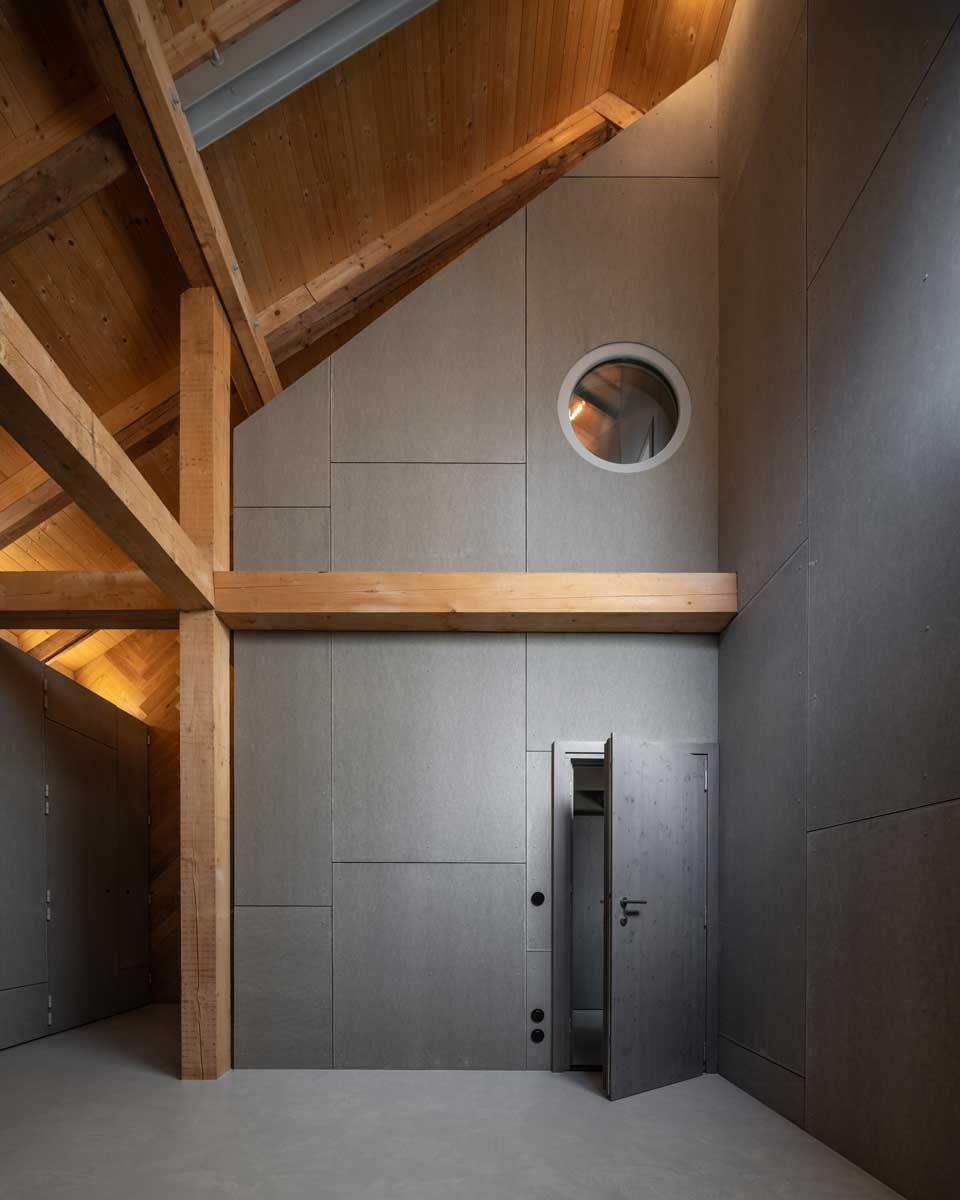 Interiér stodoly s přiznanými dřevěnými trámy a moderní vestavbou z vláknocementových desek