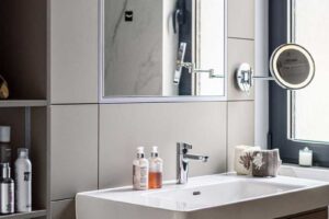 Moderní koupelna s umyvadlovou skříňkou v šedém odstínu, zrcadlovými plochami a čistými liniemi v kombinaci světlých materiálů.