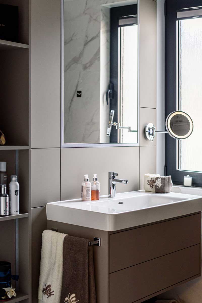 Moderní koupelna s umyvadlovou skříňkou v šedém odstínu, zrcadlovými plochami a čistými liniemi v kombinaci světlých materiálů.