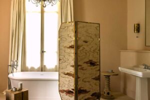 Elegantní koupelna s volně stojící vanou, historickým lustrem a textilním paravánem