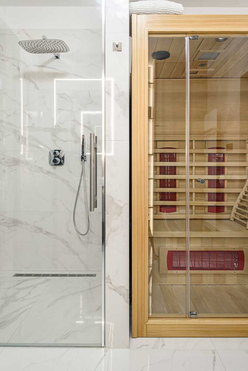 Koupelna se sprchovým koutem a vestavěnou saunou, obložená světlým mramorovým dekorem a dřevem v přírodním odstínu.