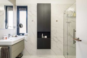 Prostorná koupelna se sprchovým koutem, skleněnými příčkami a vestavěnými úložnými skříňkami v tmavém provedení.