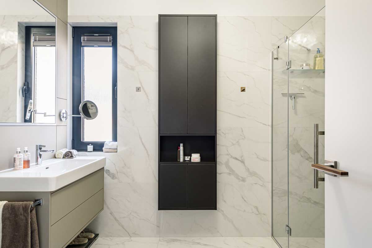 Prostorná koupelna se sprchovým koutem, skleněnými příčkami a vestavěnými úložnými skříňkami v tmavém provedení.