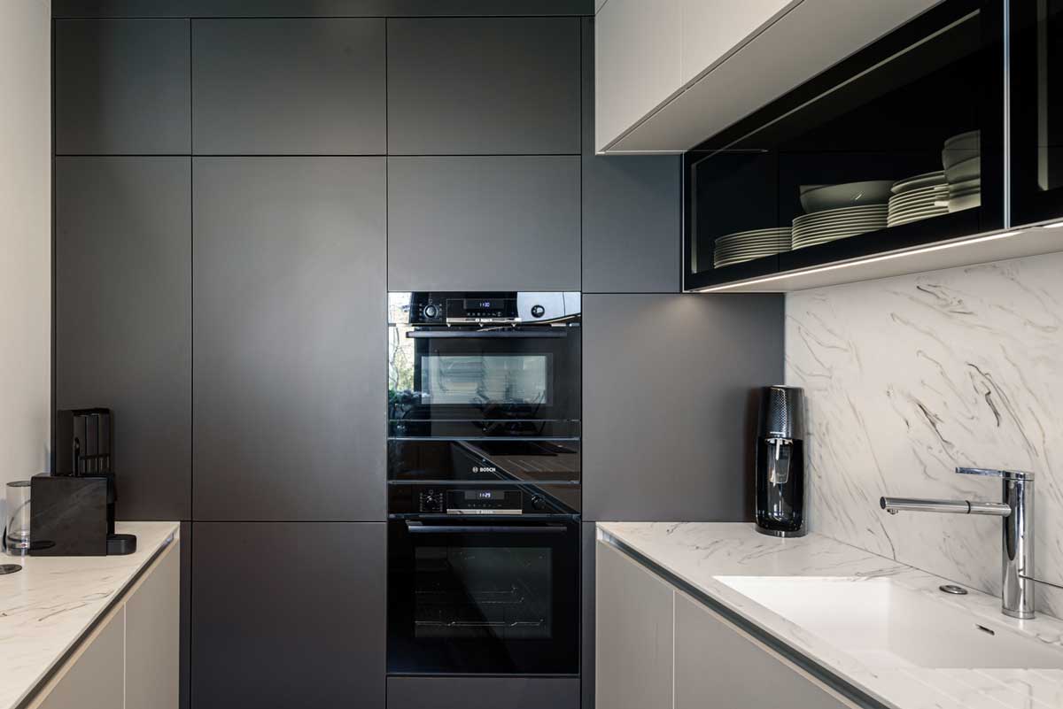 Kuchyň s vestavěnými spotřebiči, hladkými šedými skříňkami a pracovní deskou v mramorovém dekoru.