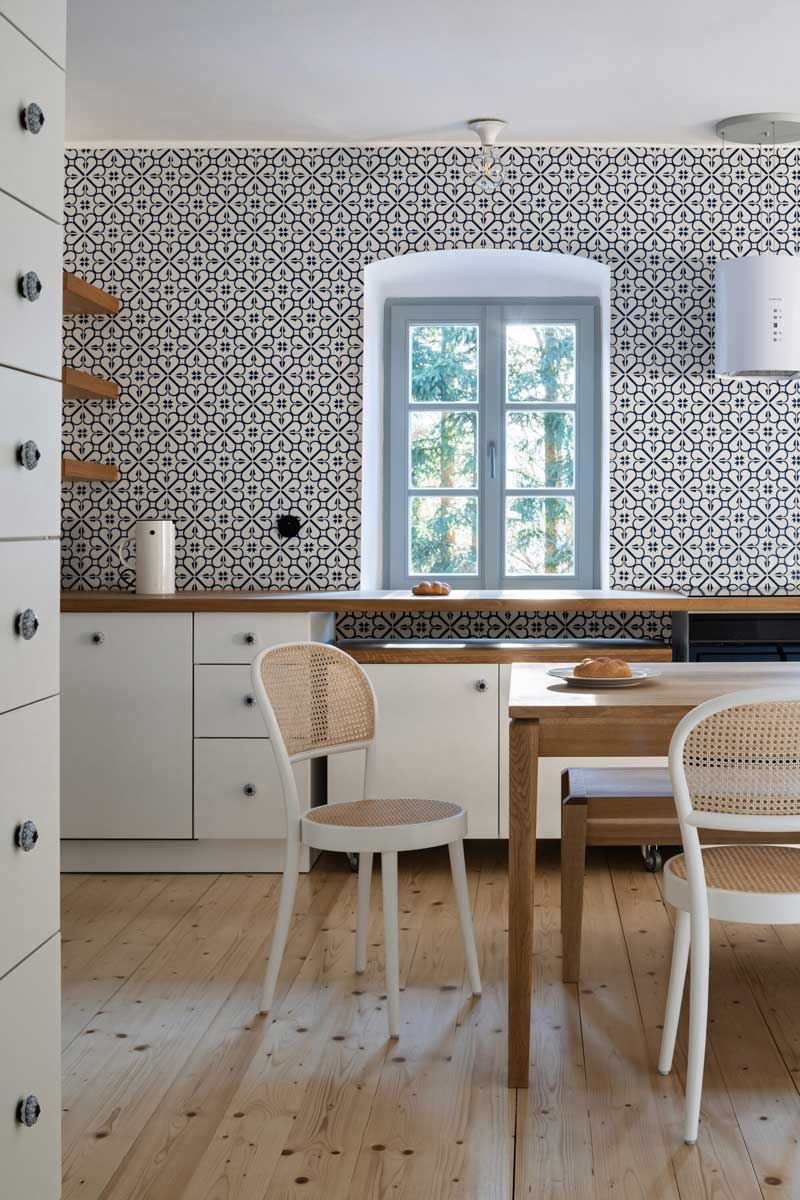 Kuchyně v chalupě s tradičními skříňkami vzorovaným obkladem a dřevěnou pracovní deskou