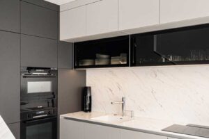 Detail kuchyňské linky s integrovaným dřezem, světlou pracovní deskou a horními skříňkami s prosklením.