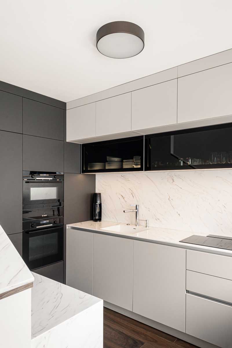 Detail kuchyňské linky s integrovaným dřezem, světlou pracovní deskou a horními skříňkami s prosklením.