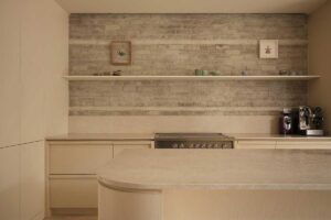 Kuchyňská linka s otevřenými policemi, světlými skříňkami a cihlovým obkladem v rekonstruovaném interiéru