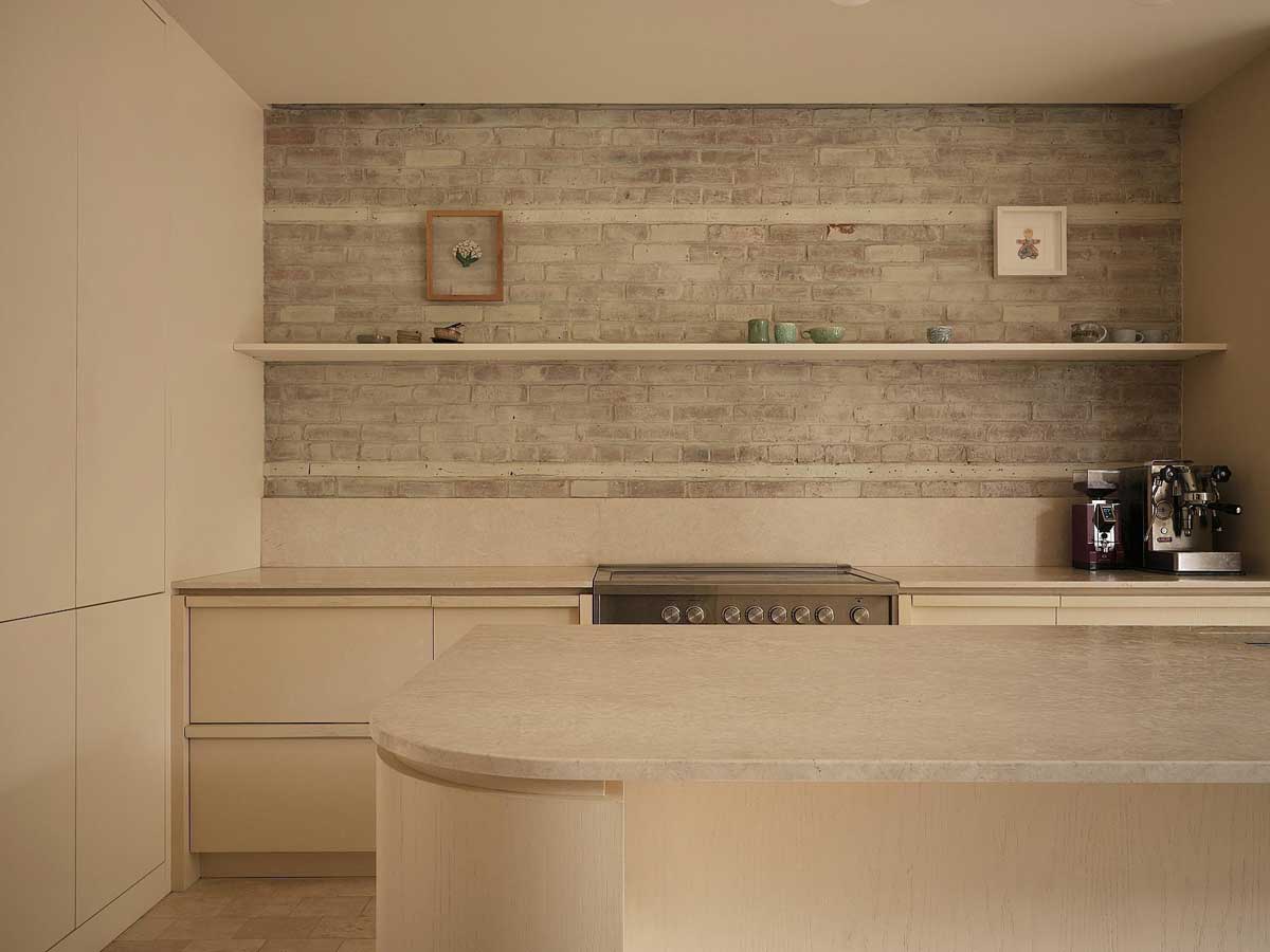 Kuchyňská linka s otevřenými policemi, světlými skříňkami a cihlovým obkladem v rekonstruovaném interiéru