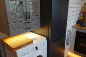 Malá paneláková kuchyně s pračkou vedle lednice a kuchyňskou linkou do tvaru L