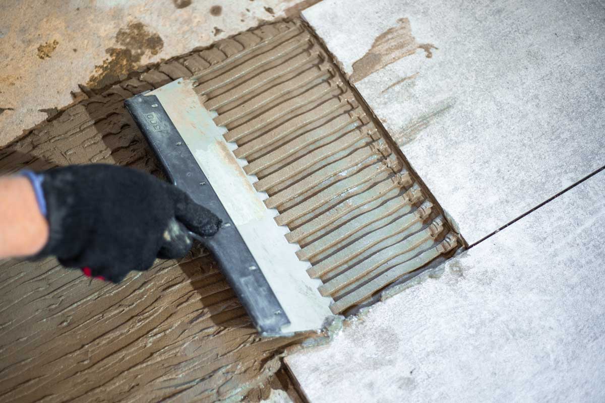 Nanášení flexibilního cementového lepidla zubovou stěrkou při lepení nového obkladu na staré kachličky