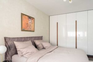 Ložnice s čalouněným čelem postele, světlými textiliemi a vestavěnou skříní s ořechovými madly.