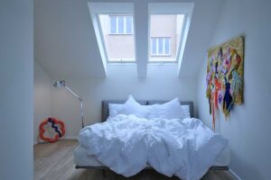 Podkrovní ložnice v pavlačovém domě se střešními okny a důrazem na přirozené denní světlo