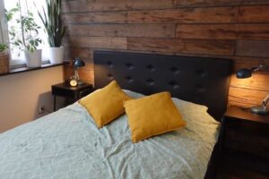 Malá ložnice s černým čelem postele a stěnou obloženou zestařeným dřevem