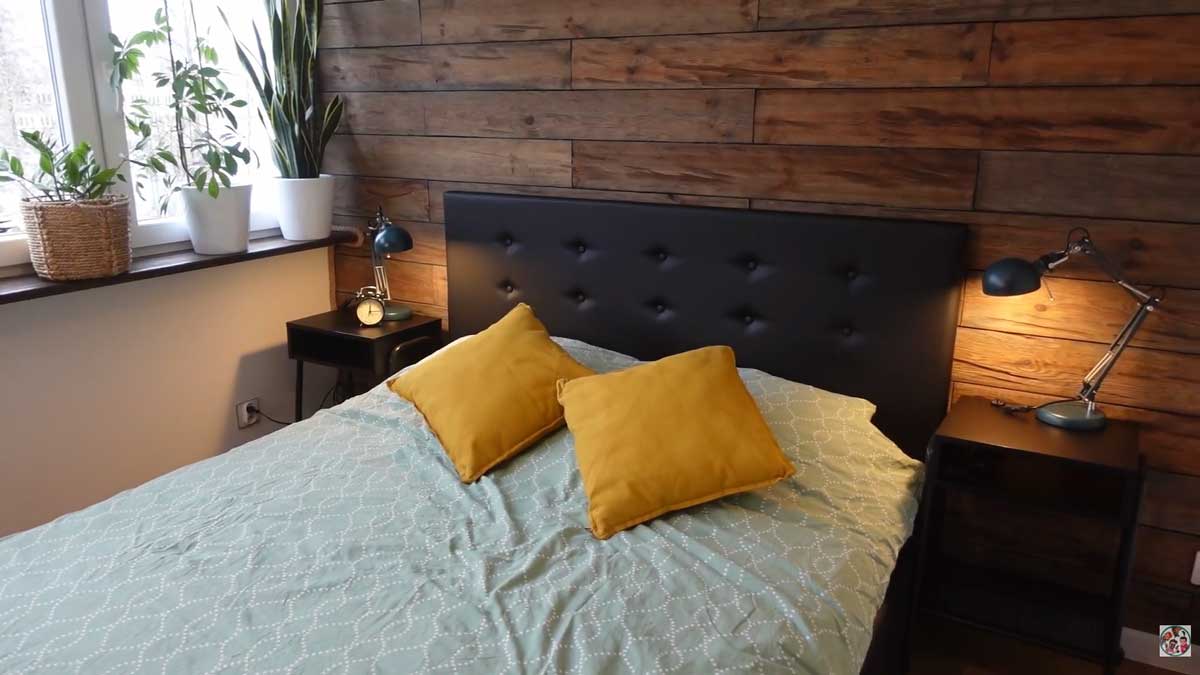 Malá ložnice s černým čelem postele a stěnou obloženou zestařeným dřevem