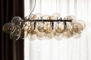 Detail designového lustru ze skleněných baněk zavěšeného nad jídelním stolem.