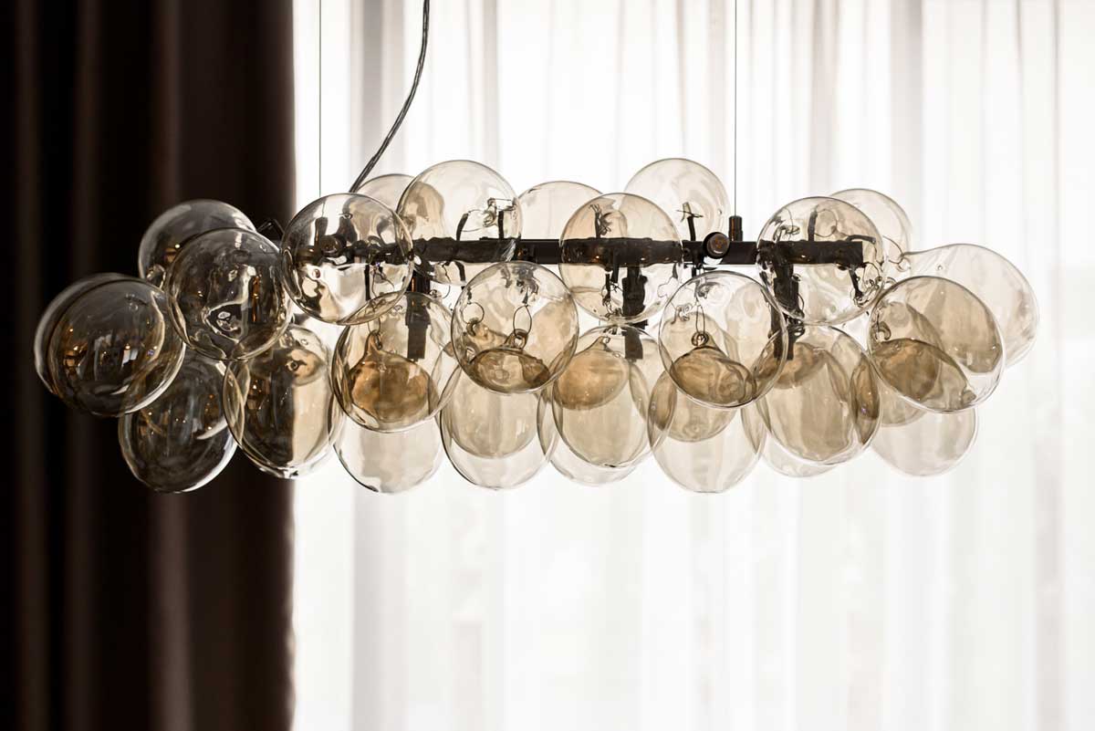 Detail designového lustru ze skleněných baněk zavěšeného nad jídelním stolem.