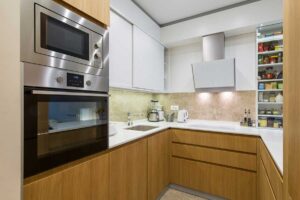 Moderní kuchyně s vestavnou troubou a mikrovlnnou troubou z nerezu, na kterých jsou viditelné otisky prstů a šmouhy od rukou.