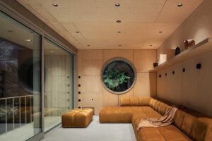 Obývací pokoj ve stodole večer s teplým osvětlením a kruhovým oknem do lesa