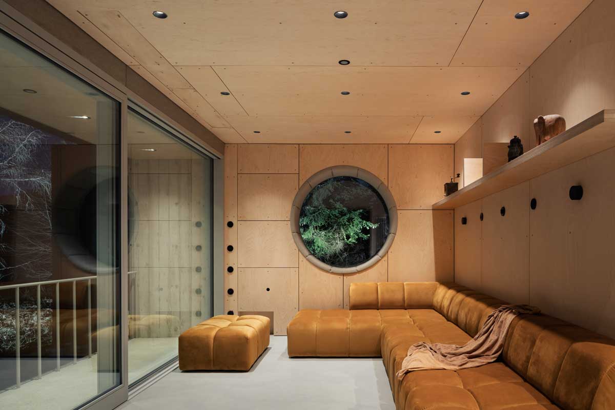 Obývací pokoj ve stodole večer s teplým osvětlením a kruhovým oknem do lesa