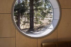 Detail kruhového okna v interiéru s výhledem na šumavské stromy