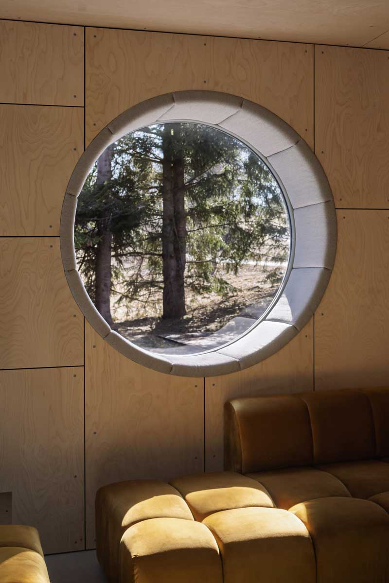 Detail kruhového okna v interiéru s výhledem na šumavské stromy