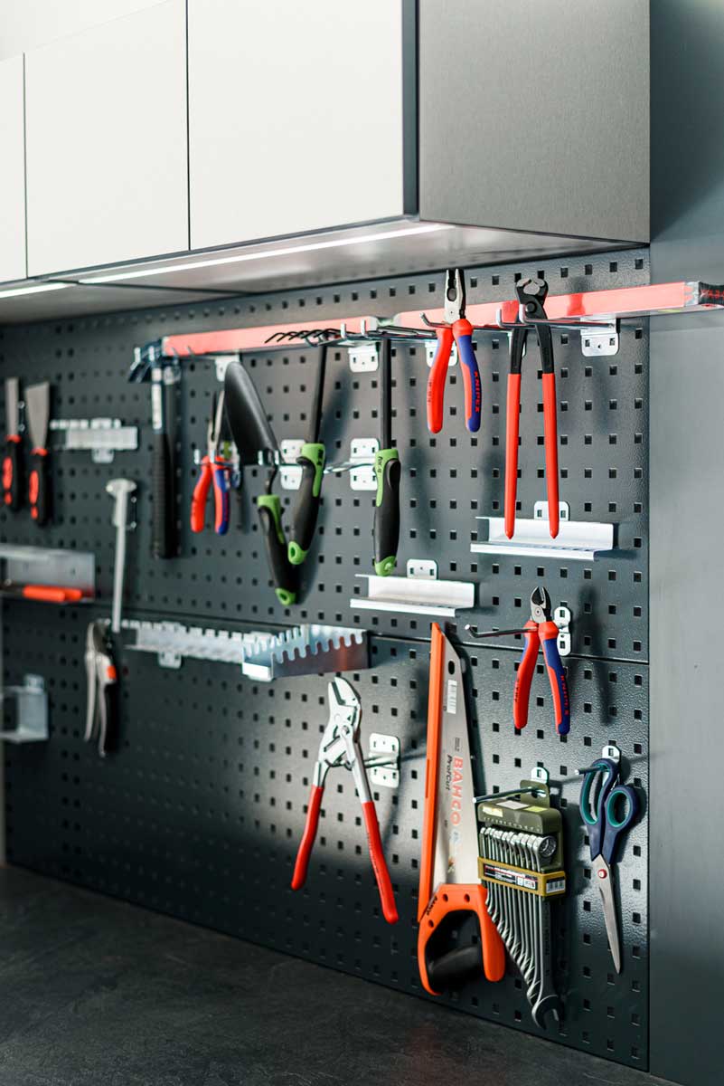 Detail organizace nářadí na perforované kovové stěně v garáži s vestavěným pracovním zázemím.