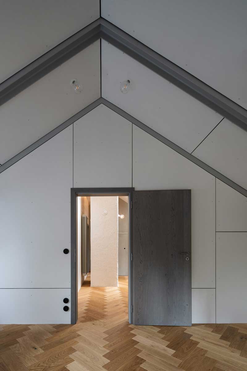 Detail podkroví s dřevěnými parketami šikmým stropem a vestavěnými dveřmi