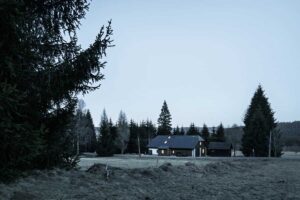 Pohled na šumavskou chalupu a stodolu v otevřené krajině při soumraku