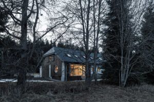 Rekonstruovaná chalupa a stodola pohledem z lesa mezi stromy