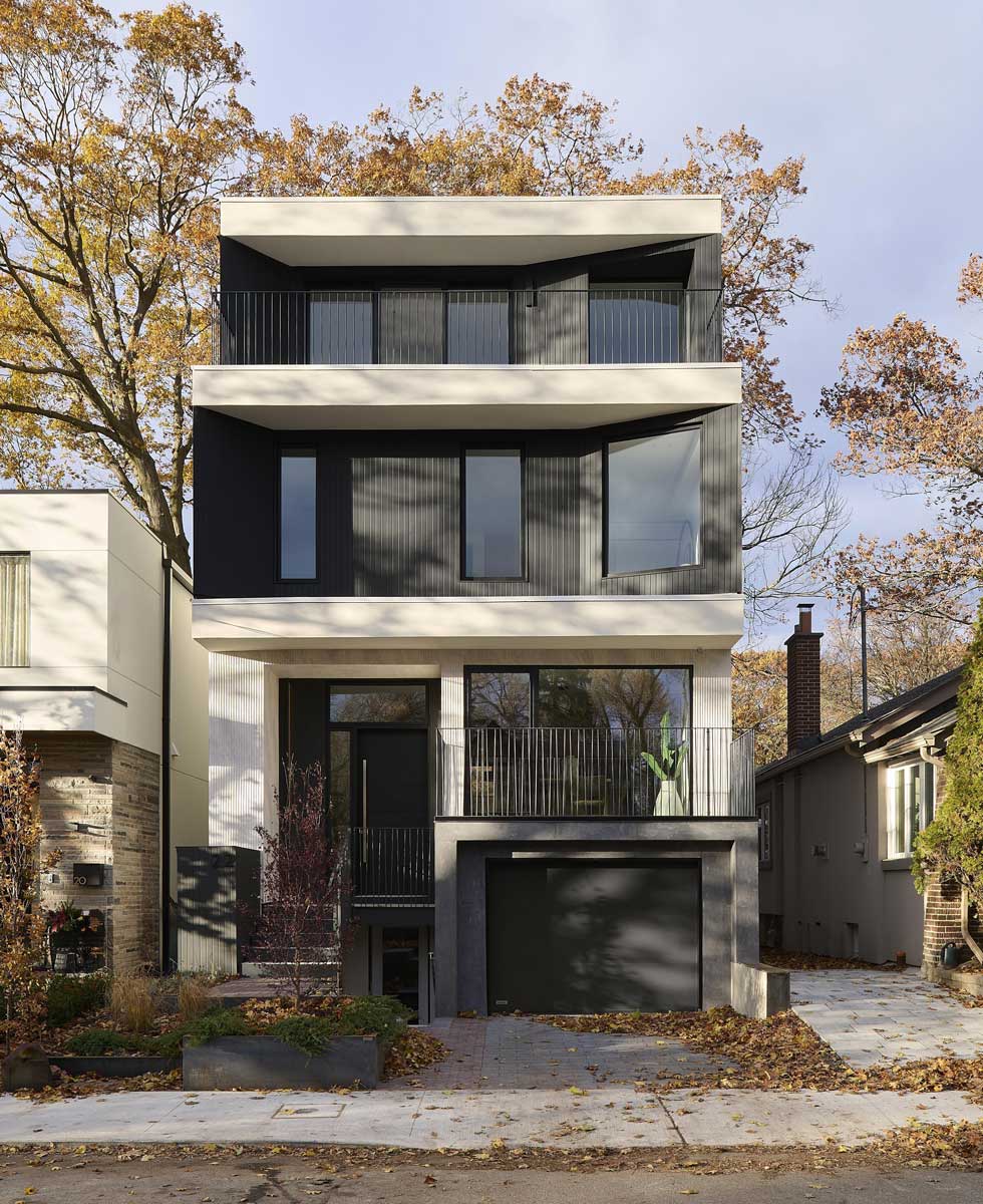 Pohled na moderní rodinný dům z ulice s tmavě mořeným dřevem, zapuštěnými balkony a střídmou fasádou