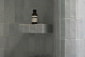Vestavěné police ve sprchovém koutě s keramickým obkladem v jemném barevném tónu