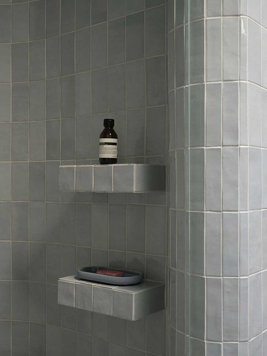 Vestavěné police ve sprchovém koutě s keramickým obkladem v jemném barevném tónu